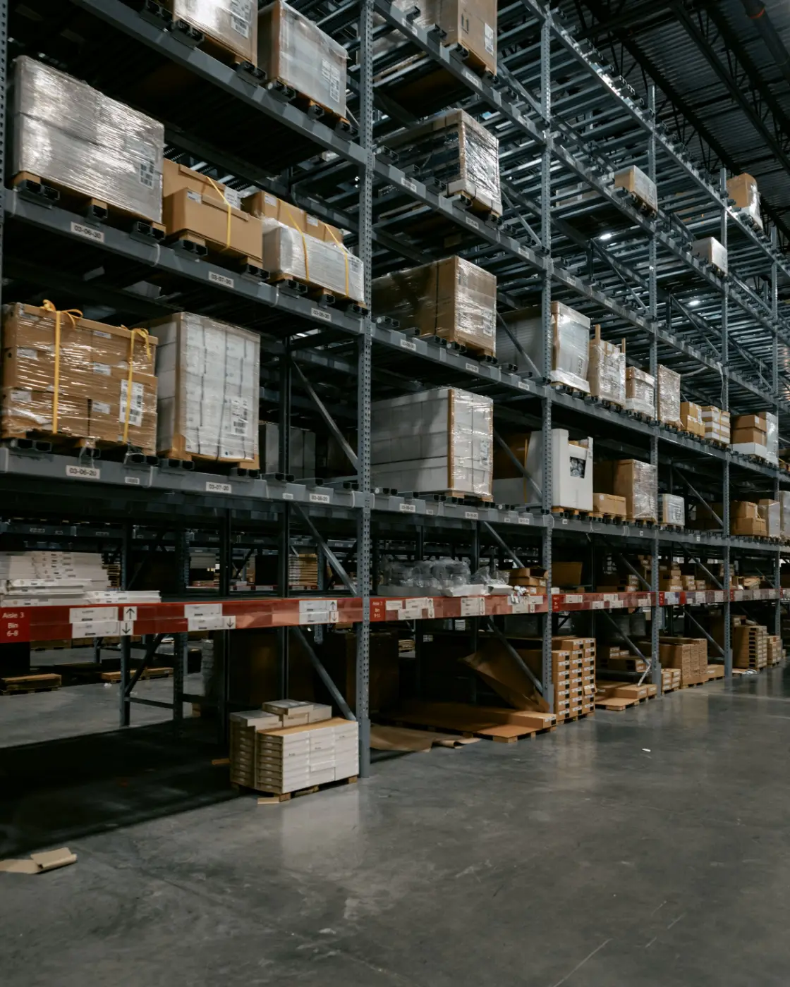 Organized warehouse racks holding pallets and cartons of product.
