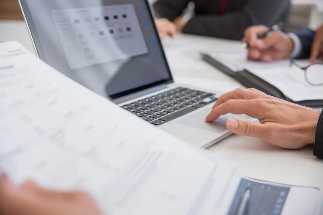 Close-up of printed documents being reviewed beside a laptop.