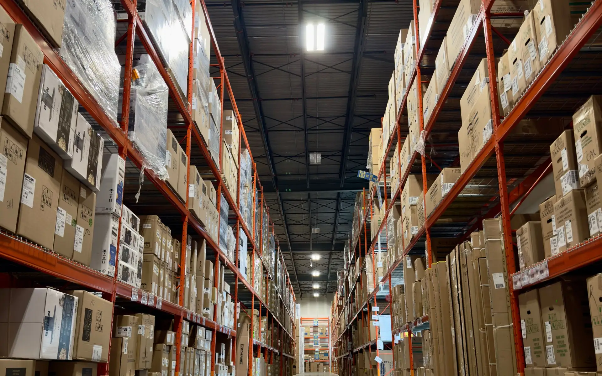 A long, well-stocked warehouse aisle with boxed product on tall racks.
